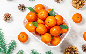 Много спелых мандаринов в белой корзинке на столе с шишками