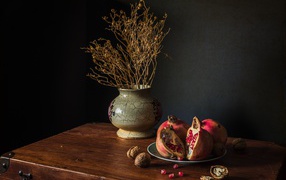 Красный гранат на столе с грецкими орехами и сухой веткой в вазе