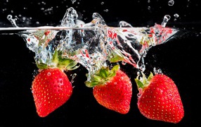 Три ягоды клубники в воде на черном фоне