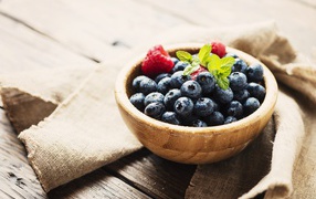 Мокрые ягоды черники в деревянной миске с малиной 