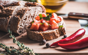 Black bread with slices of tomato on a table with hot red pepper