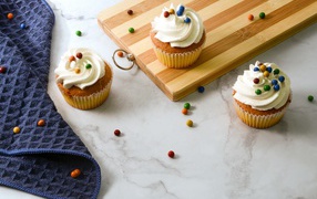 Cupcakes with cream and colorful balls on a table with a board