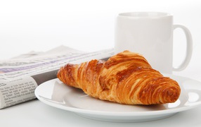 Fresh croissant lies on a white plate with coffee