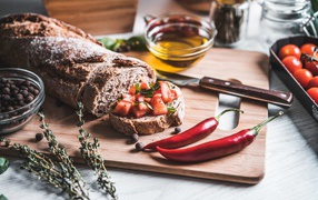 Батон с помидорами и красным перцем на столе с маслом