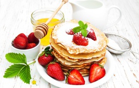 Thin pancakes with icing sugar and strawberries on a table with milk and honey