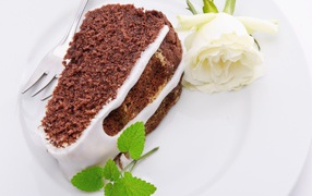 Кусок шоколадного пирога на тарелке с белой розой 