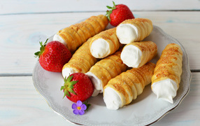 Пирожные трубочки с кремом и ягодами клубники на тарелке 