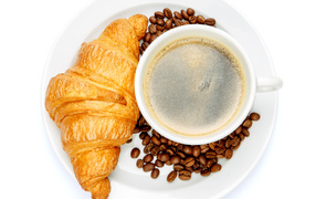 Чашка кофе на белой тарелке с круассаном и зернами, вид сверху 