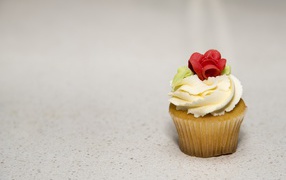 Кекс с кремом и сахарной розой на сером фоне