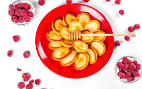 Оладьи на красной с медом на красной тарелке на столе с ягодами малины