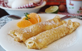 Блины с сахарной пудрой на тарелке с дольками мандарина