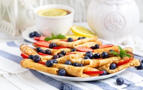 Тонкие блинчики с ягодами черники и клубники на столе с чаем