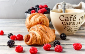 Два круассана с малиной, черникой и чашкой кофе на столе