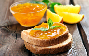 Два кусочка хлеба с апельсиновым джемом на столе с мятой