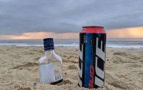 Бутылка пива и бутылка водки на песке у моря