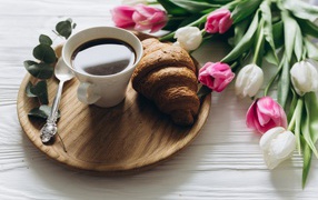 Чашка кофе и круассан на столе с букетом тюльпанов