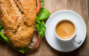 Чашка кофе с бутербродом на столе к завтраку 