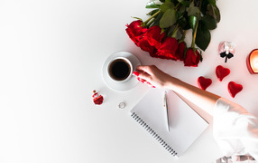 Девушка держит в руках чашку кофе на столе с блокнотом и букетом роз 