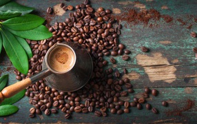 Турка с кофе на столе с зернами и зелеными листьями