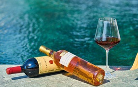 Две бутылки вина и бокал у бассейна