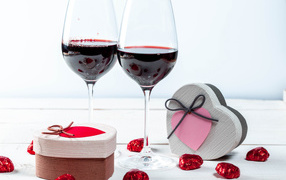 Две коробки с конфетами в форме сердца на столе с бокалами 