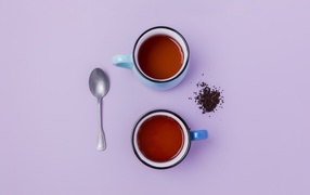 Две железные чашки чая на сиреневом фоне с ложкой