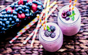 Две банки смузи с трубочками на столе с ягодами