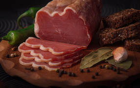 Кусок вяленого мяса на доске с черным хлебом и специями