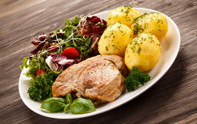 Кусок мяса на тарелке с картофелем и салатом