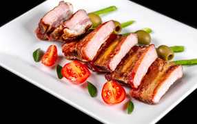 Запеченные ребрышки на белой тарелке с помидорами и оливками