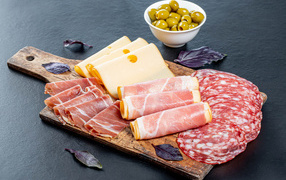 Сыр, бекон и колбаса на разделочной доске на столе с оливками