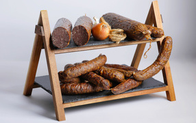 Различные виды колбасы на полке с луком на сером фоне