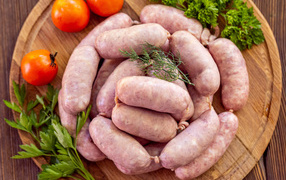 Свежие сырые домашние сардельки на доске с петрушкой и помидорами