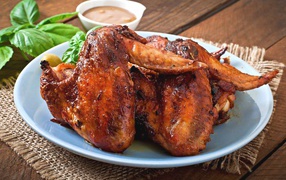 Зажареные куриные крылышки на столе с соусом и базиликом