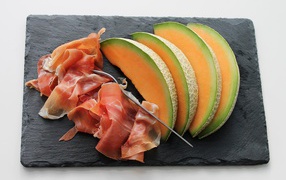 Кусочки дыни на доске с прошутто