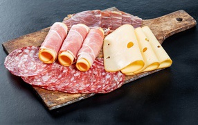 Куски сыра, ветчины и колбасы на доске