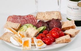 Тарелка с мясными продуктами, яйцами, овощами и хлебом на столе с вином
