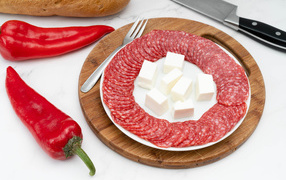 Тарелка с колбасой и сыром на столе с красным перцем