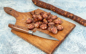 Колбаса нарезана колечками на разделочной доске с ножом 