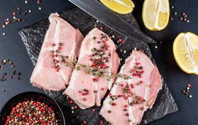 Куски свежего мяса на столе с зернами перца и лимоном