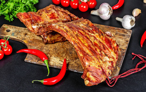 Копченые ребра на столе с красным перцем, чесноком и помидорами