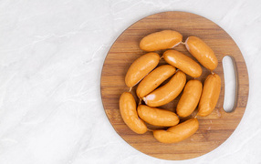 Копченые сардельки на деревянной доске на сером фоне