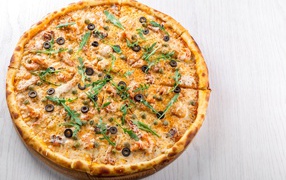 Пицца с морепродуктами, рукколой и оливками на столе 