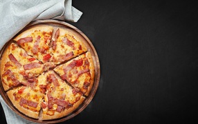 Pizza with slices of bacon on a blackboard on a black background