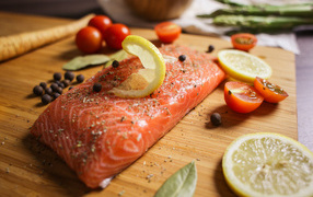 Кусок красной рыбы на доске с лимоном и помидорами