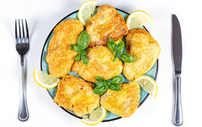 Аппетитная рыба в кляре на тарелке с кусочками лимона и столовыми приборами