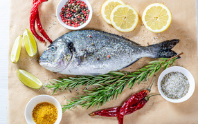 Свежая рыба на столе со специями, лимоном, розмарином и красным перцем