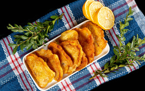 Жареная рыба в кляре на столе с лимоном и зеленью