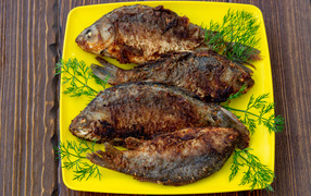 Жареные караси с укропом на желтой тарелке 