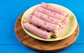 Рулетики из ветчины на тарелке на голубом столе